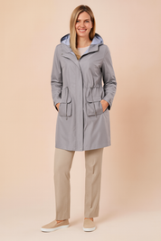 Light grey hooded raincoat with striped hood lining, front zipper, adjustable waist drawcord, and two large flap pockets, paired with straight-leg beige trousers and beige slip-on shoes.

