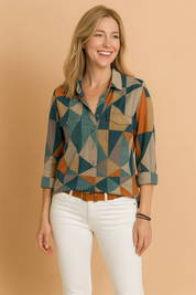 Color-block button-down shirt with bold geometric triangle patterns in deep teal, burnt orange, sand beige, and slate grey, paired with fitted white jeans and a tan leather belt.