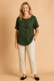 Forest green short-sleeve linen blouse with round neckline and diagonal button detailing, styled with off-white straight-leg pants.