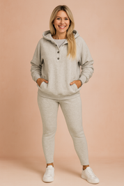 Heather gray lounge set featuring a hooded pullover with three dark buttons, paired with matching slim-fit leggings and white low-top sneakers; made of soft fleece-like fabric for cozy everyday wear.