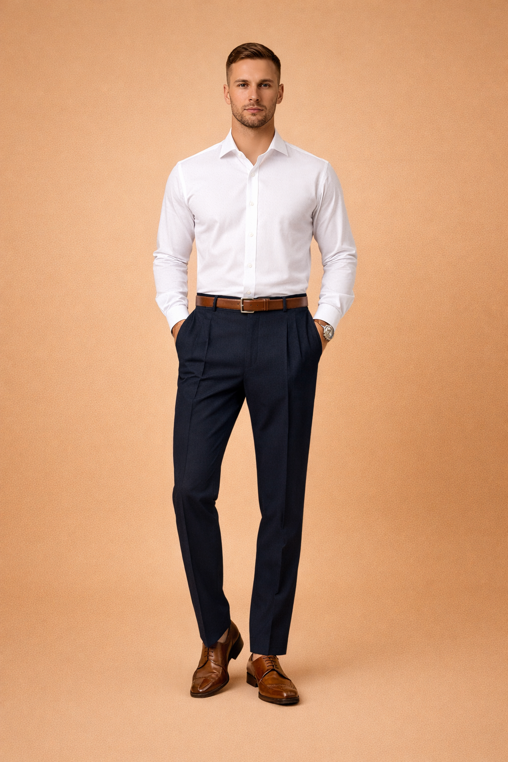 Men’s tailored navy dress trousers with clean front pleats and slim straight-leg cut, styled with a crisp white long-sleeve shirt, brown leather belt, and polished brown lace-up dress shoes