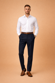 Men’s tailored navy dress trousers with clean front pleats and slim straight-leg cut, styled with a crisp white long-sleeve shirt, brown leather belt, and polished brown lace-up dress shoes