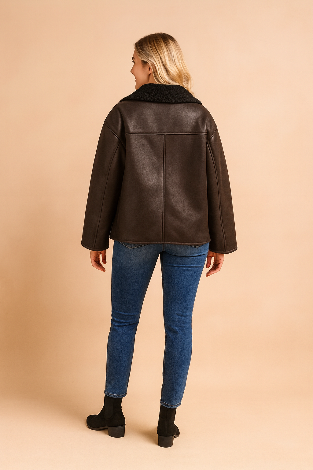 Back view of a dark brown shearling-lined jacket with wide sleeves, straight hem, and panel seam detailing, featuring a soft textured interior collar and smooth leather-look exterior.