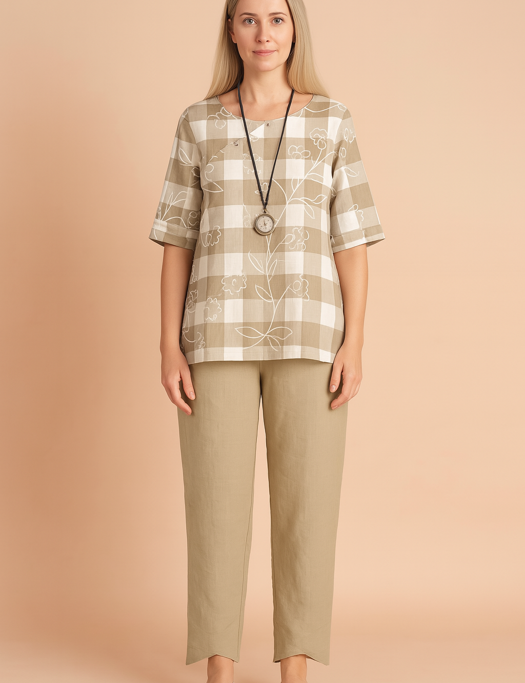 Beige and white plaid tunic with floral outlines paired with high-waisted beige tapered trousers featuring asymmetrical cuffs, styled with a round pendant necklace and neutral slip-on footwear.