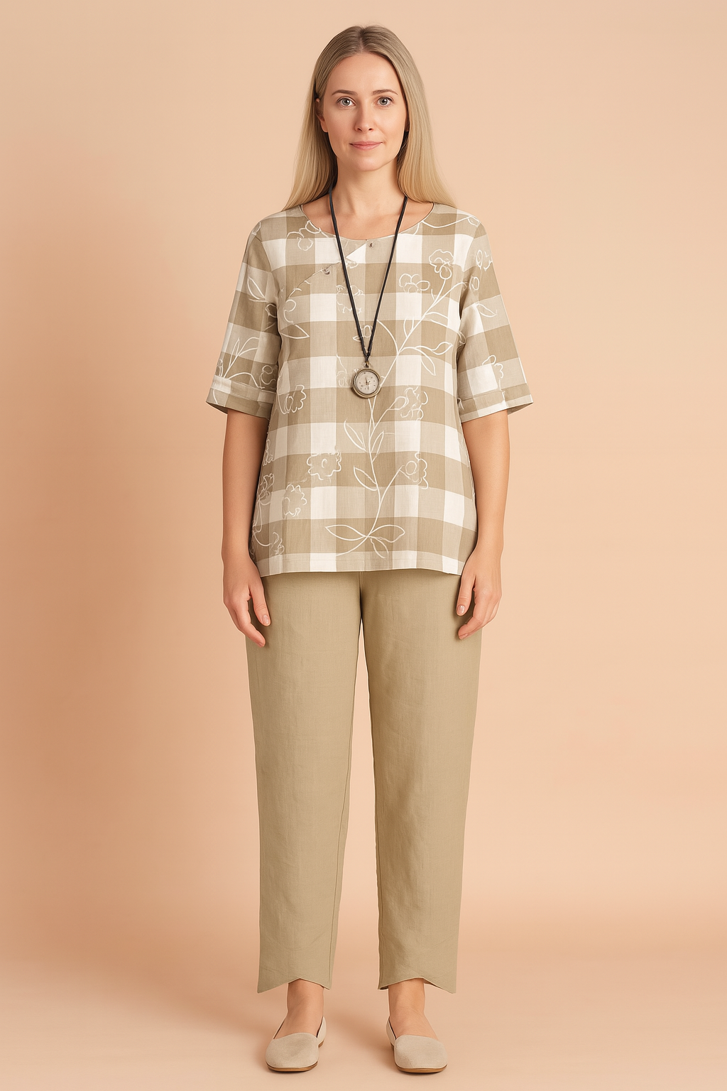 Beige and white plaid tunic with floral outlines paired with high-waisted beige tapered trousers featuring asymmetrical cuffs, styled with a round pendant necklace and neutral slip-on footwear.