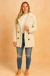 Beige double-breasted teddy-texture coat with wide lapels, paired with white ribbed turtleneck, ripped skinny jeans, and beige heel