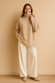 Oversized beige turtleneck sweater with ribbed hem and cuffs, styled with high-waisted cream trousers and beige ankle boots for a warm neutral-toned outfit.