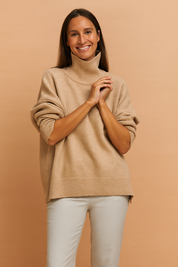 Beige oversized turtleneck sweater with ribbed hem and cuffs, styled with light taupe slim-fit trousers in a cozy neutral-toned ensemble