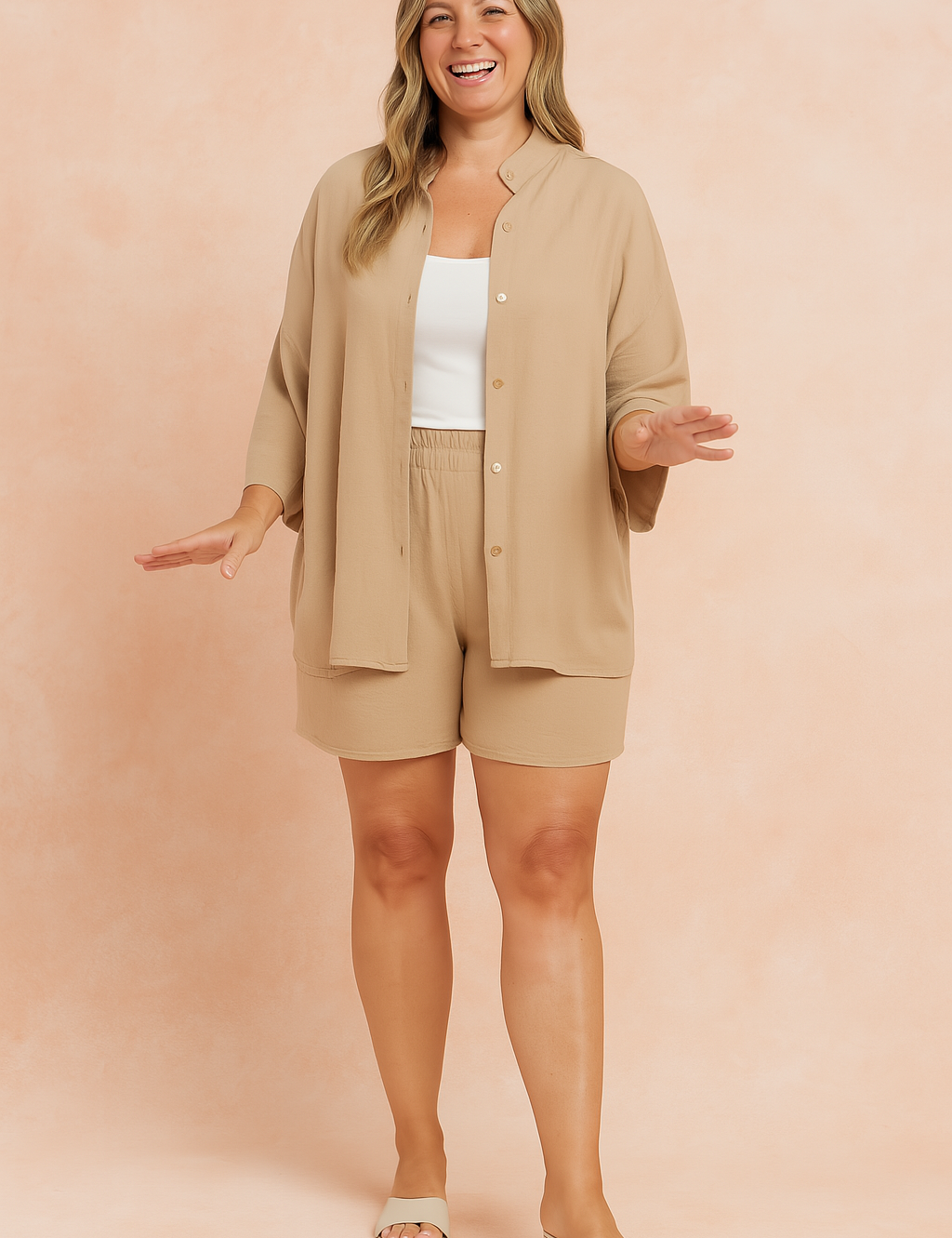Beige oversized button-up shirt with dropped shoulders paired with matching high-waisted loose shorts in soft, flowy fabric; styled over a white cropped tank top.