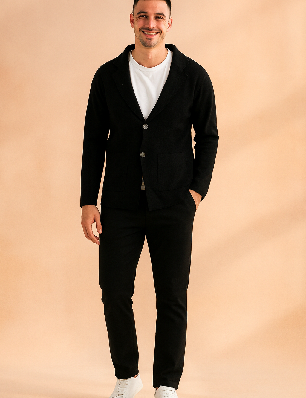 Black two-button blazer-style cardigan with front patch pockets, styled over a white T-shirt, slim black trousers, and white sneakers for a modern casual look.