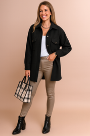 Black button-up jacket with flap chest pockets and matching buttons, styled over a white top, beige slim-fit pants, black ankle boots, and a plaid tote bag.