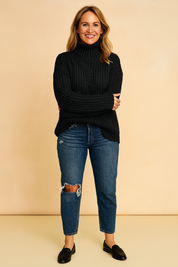 Black cable-knit turtleneck sweater with textured detailing, paired with distressed medium-wash jeans and black leather loafers for a casual winter street look.