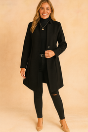 Tailored long black coat with structured lapels, single-breasted design, styled with black turtleneck, fitted jeans, and beige heels.
