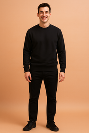Men's classic black crewneck sweatshirt with long sleeves and ribbed cuffs, styled with straight black trousers and matching black sneakers for a clean, modern casual outfit.