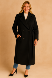Elegant black double-breasted long coat with structured lapels and side pockets, styled with a white turtleneck, slim-fit jeans, and classic heels.