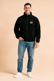 Black fleece zip-up jacket with a high collar, chest logo patch, and front pockets, styled casually with jeans and sneakers for a modern outdoor look.