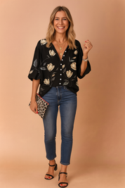 Black button-up blouse with wide three-quarter sleeves, featuring a soft ivory and gray floral print, paired with fitted mid-rise blue jeans and classic black heeled sandals.