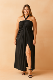 Black halter-neck maxi dress featuring a twisted knot at the neckline and flowing draped fabric with a soft paisley texture, styled with a front leg slit and paired with black heeled sandals.