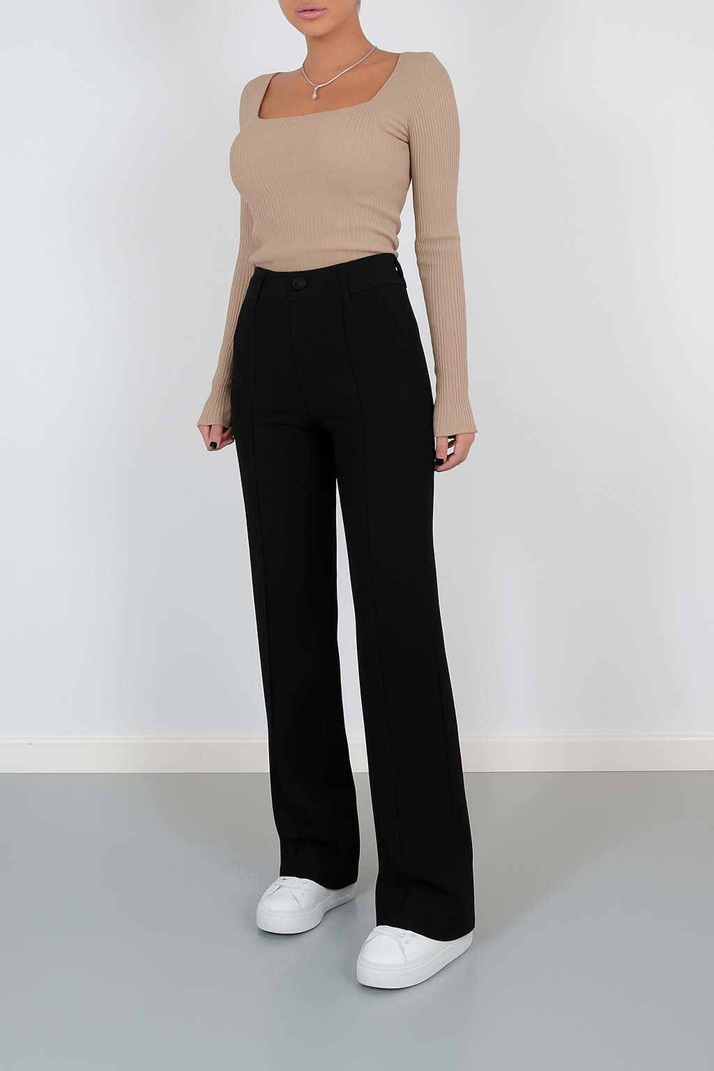 High-waisted black tailored trousers with front seam details and a wide-leg silhouette, paired with casual white sneakers for a polished minimalist look.