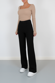 High-waisted black tailored trousers with front seam details and a wide-leg silhouette, paired with casual white sneakers for a polished minimalist look.