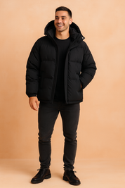 Black puffer winter jacket with detachable hood, front zipper closure, and horizontal quilted padding for enhanced insulation and urban streetwear appeal.