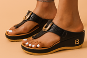 Black wedge thong sandals with perforated leather straps, gold horseshoe embellishments, and a tan-and-black layered sole featuring a metallic "B" accent on the side.
