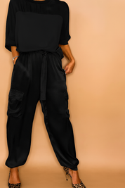 Black satin cargo pants with a relaxed fit, utility side pockets, and ankle cinching, styled with a loose black top and leopard-print pumps.
