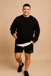 Men’s casual black long-sleeve sweatshirt paired with layered white undershirt, styled with black drawstring shorts featuring a side pocket logo print.