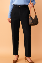 Tailored high-waisted black trousers with a sleek straight-leg cut, pressed center creases, side seam pockets, belt loops, and a single-button front closure, styled with a tucked-in light knit top and pointed-toe heels.