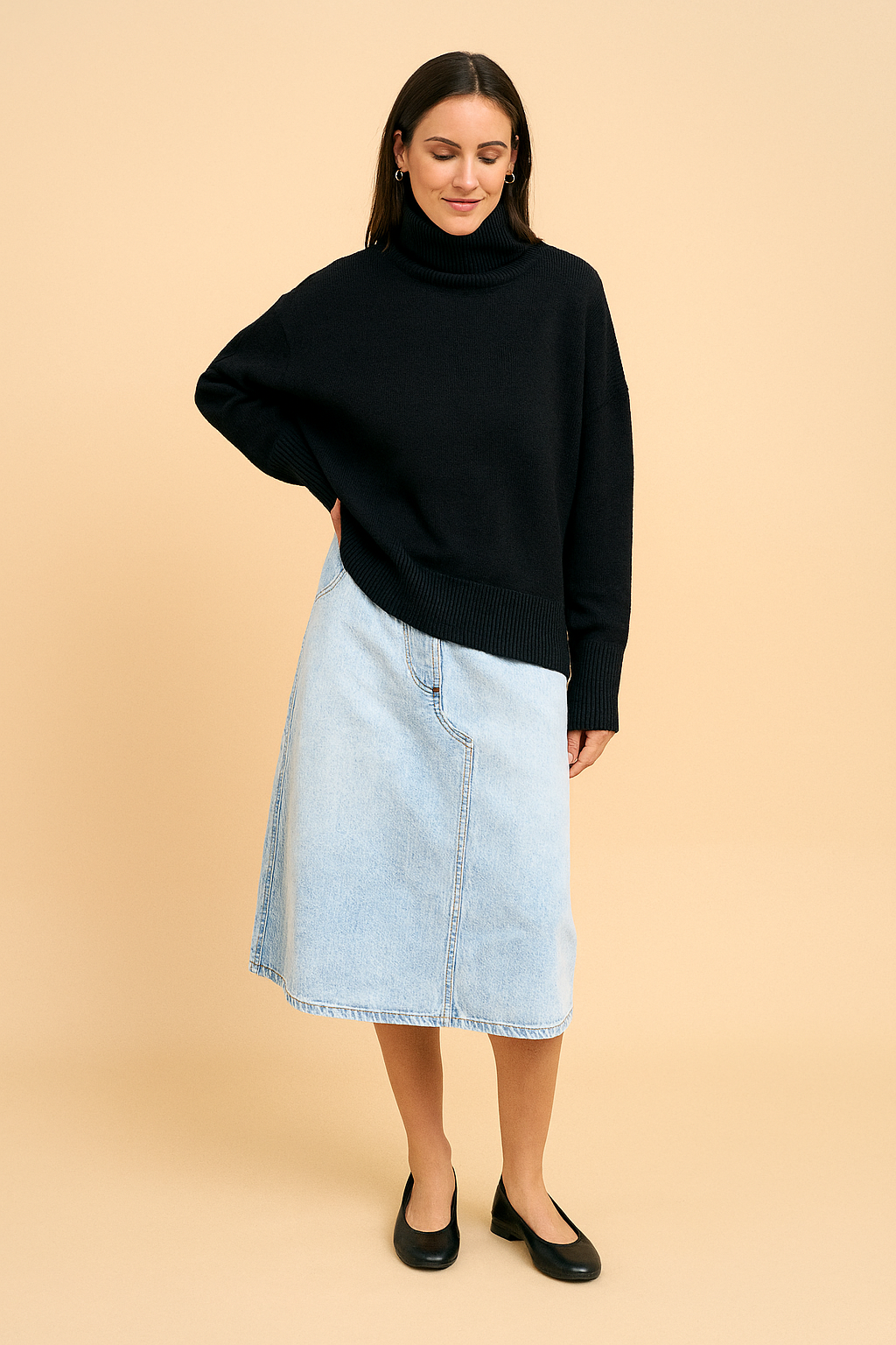 Black oversized turtleneck sweater paired with a light blue denim midi skirt and classic black ballet flats, styled with gold hoop earrings.