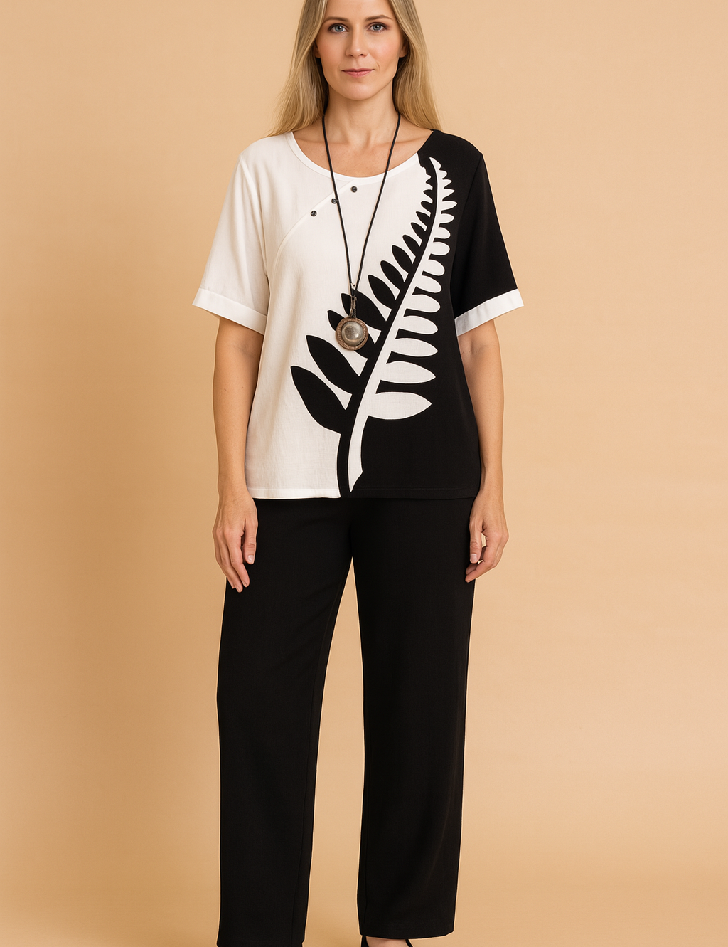 Two-piece casual outfit featuring a black-and-white split tunic top with bold fern leaf print and asymmetrical button detailing, paired with loose-fitting solid black ankle-length trousers made from soft woven fabric.