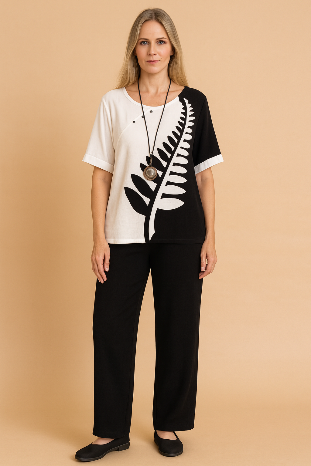 Two-piece casual outfit featuring a black-and-white split tunic top with bold fern leaf print and asymmetrical button detailing, paired with loose-fitting solid black ankle-length trousers made from soft woven fabric.
