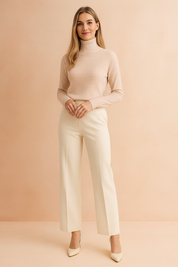 Soft blush beige fitted knit turtleneck sweater with ribbed collar and cuffs, styled with ivory wide-leg trousers and matching heels.