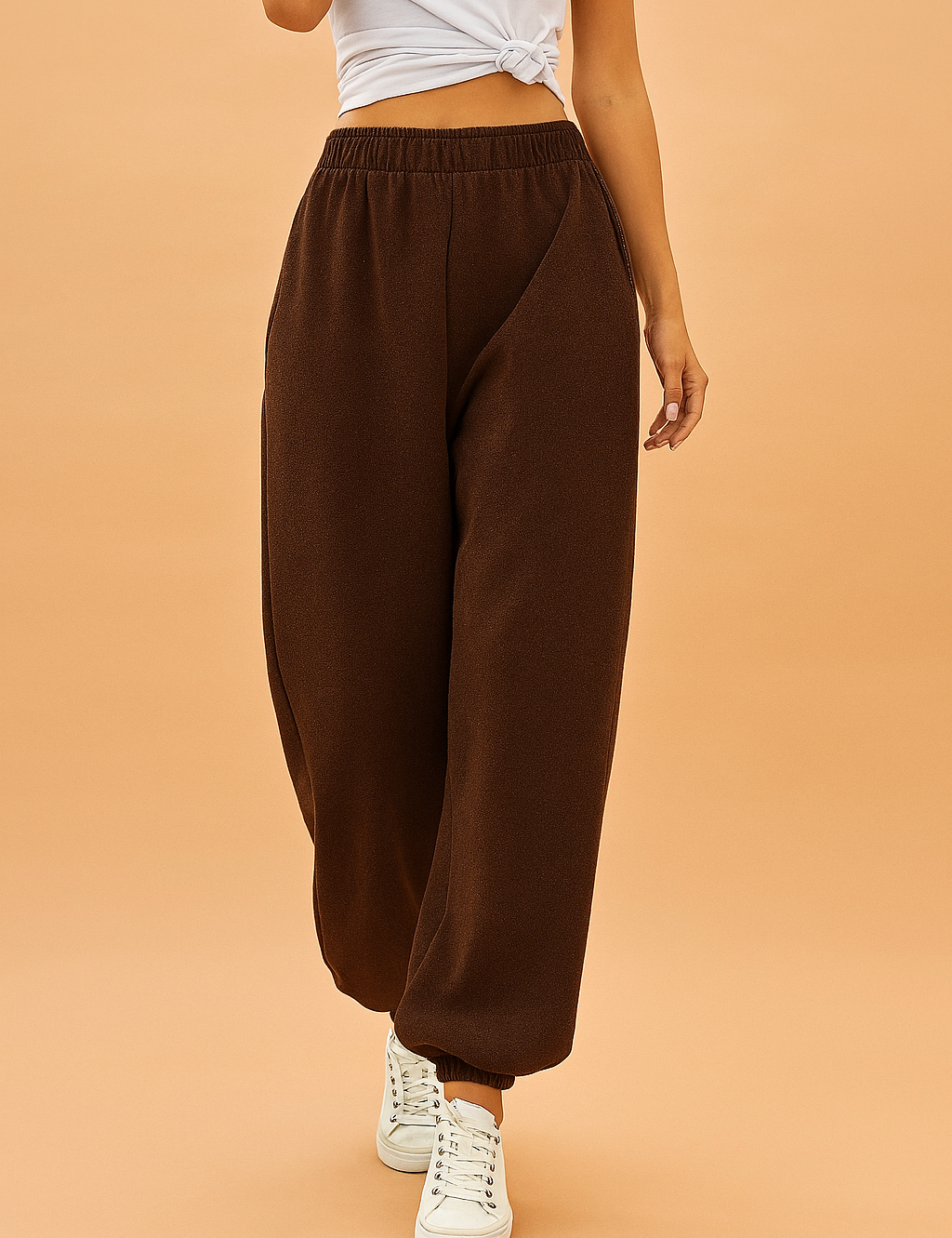 Brown jogger sweatpants with an elastic waistband and cuffed ankles, styled with white sneakers for a casual streetwear look.