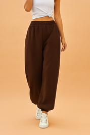 Brown jogger sweatpants with an elastic waistband and cuffed ankles, styled with white sneakers for a casual streetwear look.