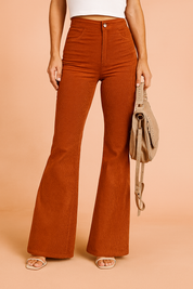 High-waisted burnt orange corduroy flare pants with a front button and zip closure, subtle vertical ridged texture, and two front pockets, styled with neutral heels and a tan crossbody bag.