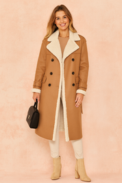 Camel shearling-lined trench coat with wide lapels and double-breasted button closure, styled with beige pants, suede ankle boots, and a structured handbag.