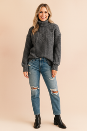 Charcoal grey chunky cable-knit turtleneck sweater paired with light blue distressed denim jeans and black ankle boots.