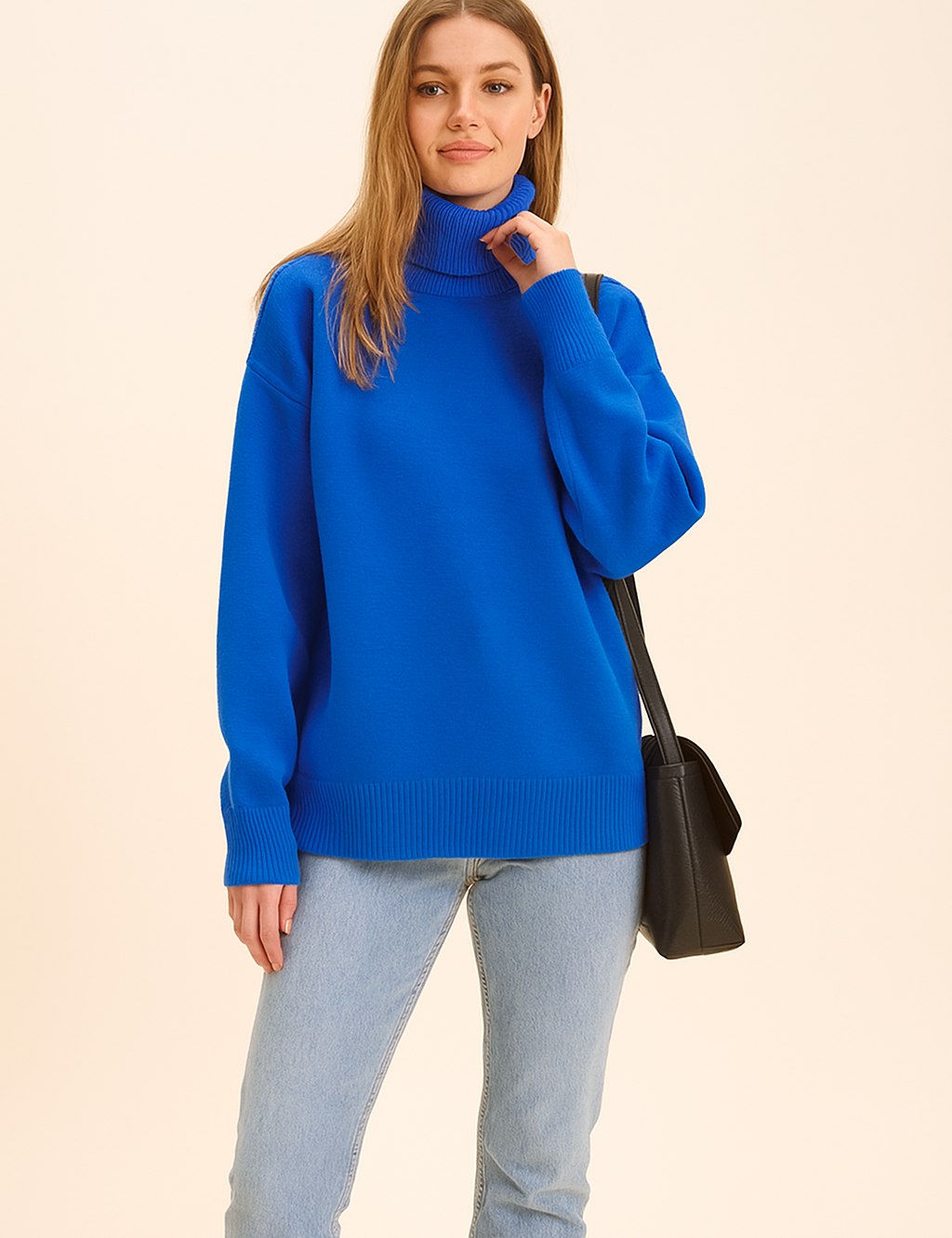Cobalt blue oversized knit turtleneck sweater with ribbed hem and cuffs, paired with light wash straight-leg jeans and black leather shoulder bag.