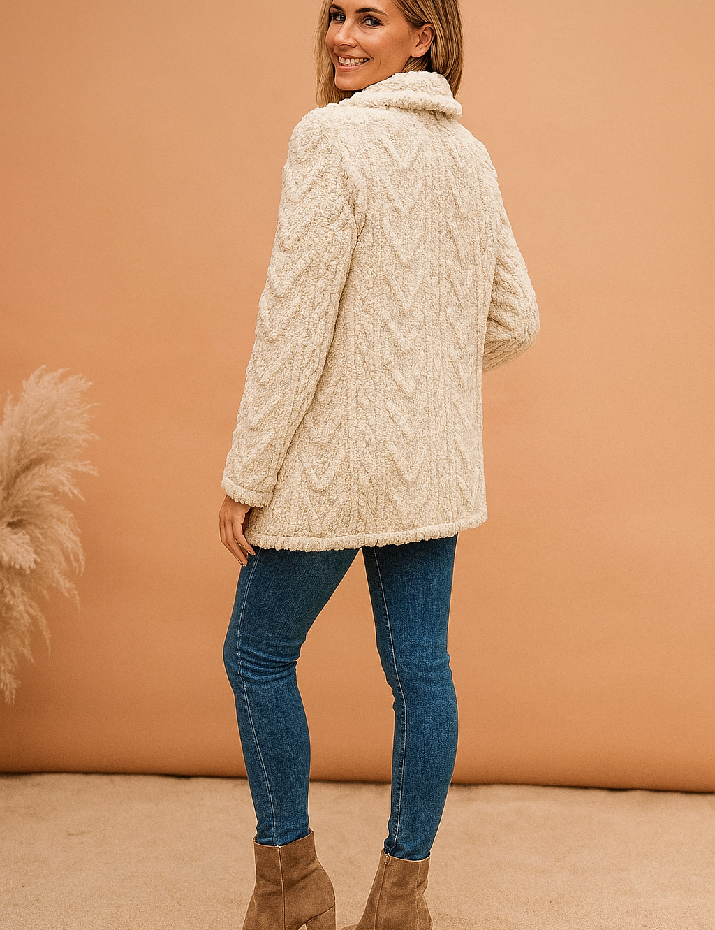 Cream textured faux shearling jacket with cable-knit pattern, featuring a soft collar and hip-length cut, paired with slim blue jeans and taupe heeled ankle boots.