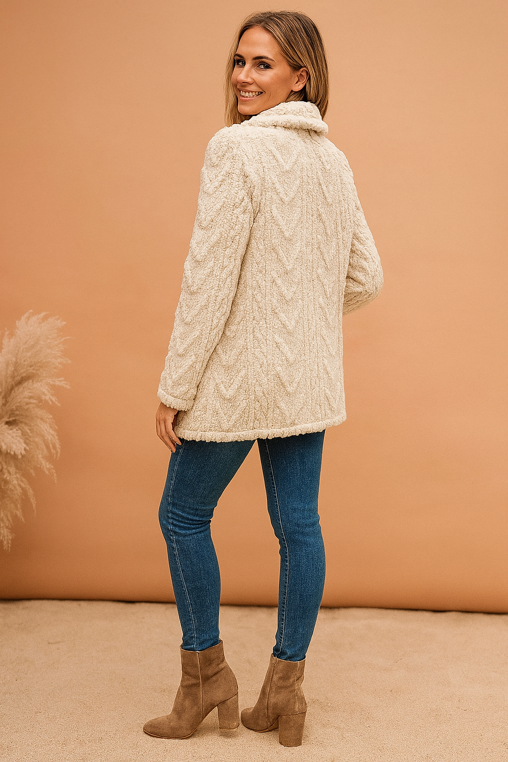 Cream textured faux shearling jacket with cable-knit pattern, featuring a soft collar and hip-length cut, paired with slim blue jeans and taupe heeled ankle boots.