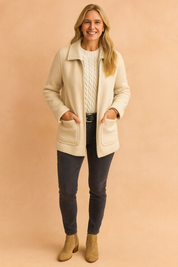 Cream fleece coat with front patch pockets layered over a white cable-knit sweater, paired with charcoal jeans, a black belt, and tan suede ankle boots.