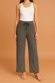 Dark gray wide-leg pleated pants with a drawstring waistband and ribbed texture, styled with a fitted white tank top and nude block-heeled sandals.
