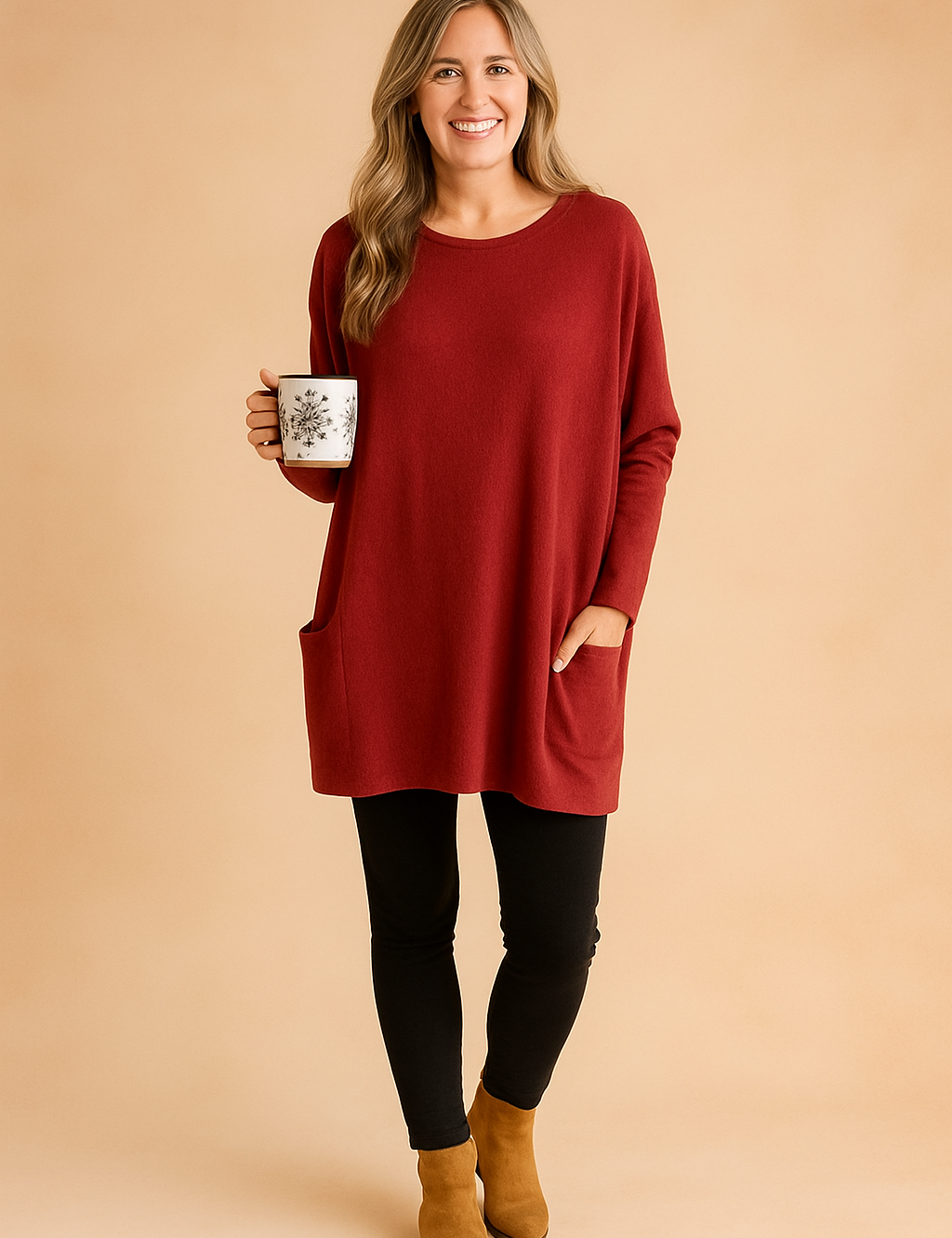 Deep red oversized tunic sweater without buttons, featuring long relaxed sleeves, front patch pockets, and soft knit texture, styled with black leggings and tan suede ankle boots.