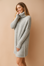 Light gray oversized chunky knit sweater dress with ribbed turtleneck and extended cuffs, showcasing soft texture and relaxed silhouette.