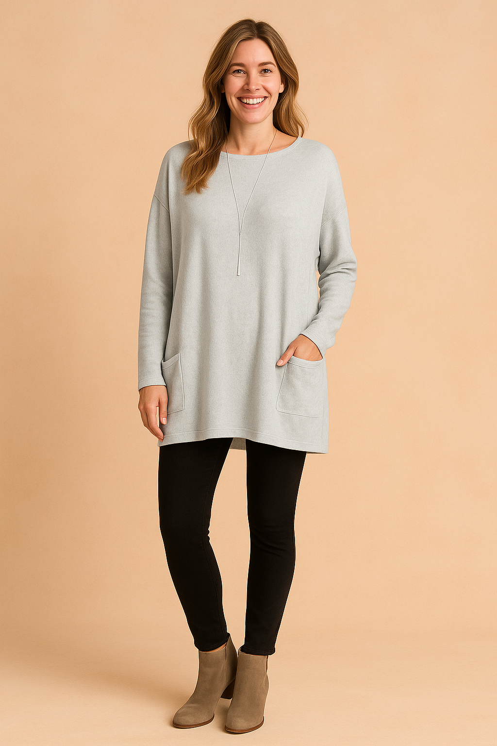 Light gray oversized long-sleeve knit tunic with front patch pockets, paired with black leggings and taupe ankle boots.