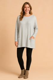 Light gray oversized long-sleeve knit tunic with front patch pockets, paired with black leggings and taupe ankle boots.