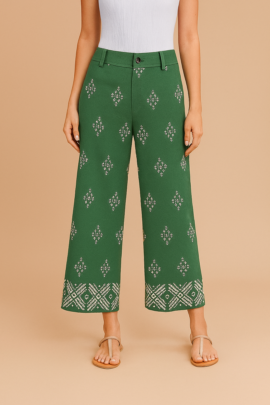 Green cropped wide-leg pants with symmetrical white geometric embroidery throughout and a detailed border pattern at the hem, featuring a high-rise waist with belt loops and front button closure, styled with beige sandals.