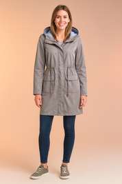 Light grey hooded raincoat with striped inner lining, front drawstring waist, snap-button closure, and two large flap pockets, styled with casual sneakers and fitted jeans.