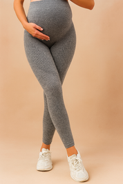 High-rise grey ribbed maternity leggings with a sculpting waistband and contoured knit detailing, paired with white athletic sneakers.
